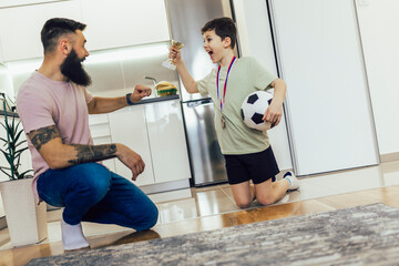 Proud father feel so excited to see his son medal and trophy in his hand after football tournament.