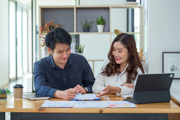 Fototapeta premium Young Asian businesswoman and businessman discuss investment project working and planning strategy at meeting. Business people talking together with tablet at office.