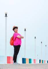 Perspective side view of Asian plus size woman smiling and looking at camera while posing on multicolor bridge at sea viewpoint after raining in pastel tone style and vertical frame