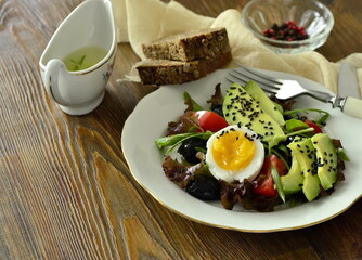 Avocado salad with olives, tomatoes, lettuce, arugula and boiled egg, copy space