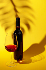 Glass and bottle of red wine on a yellow background.