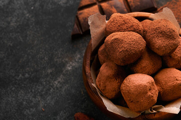 Chocolate truffles with cocoa powder in wooden dish on old dark concrete table background. Tasty sweet chocolate truffles candies. Valentines Day and Mothers Day concept with copy space. Top view.