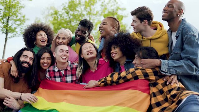 Happy diverse friends holding LGBT rainbow flag having fun together outdoors - Diversity community concept