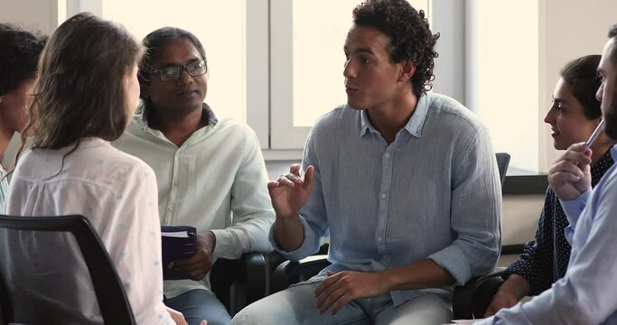 Confident Latino male leader of diverse student group offer idea set tasks for common project share plan of work with teammates. Young male manager talk to mixed race team members on office meeting