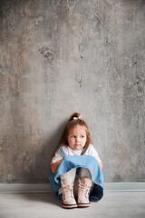 Obraz na płótnie Canvas Adorable little girl in denim dress sitting against the wall in new home.