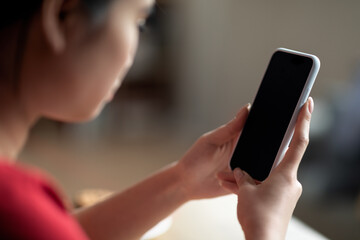 Serious young chinese woman typing on smartphone with blank screen, chatting in social networks in room