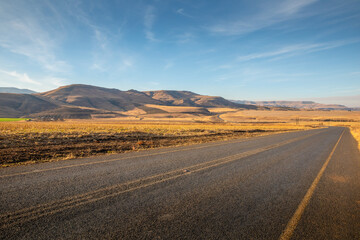 Fototapeta na wymiar A tarmac road cuts through the dry, arid landscape of Kwazulu Natal near Drakensberg, South Africa.