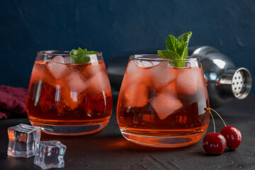 Cherry cocktail in glass on blue background. Summer iced beverage.