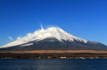Fuji mountain with snow and fog covered top, lake or sea and clear blue sky background with copy space. This place famous in Japan and Asia for people travel to visit and take picture.