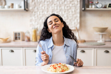 Excited lady enjoying delicious homemade pasta, eating tasty lunch with closed eyes while sitting...