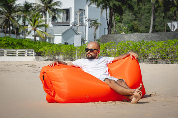 Young man relaxing on the beach while sitting on an inflatable sofa