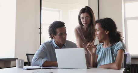 Group of three diverse office workers gather on meeting at workplace think brainstorm discuss project on laptop screen work out new sales strategy. Young multiethnic teammates collaborate on research