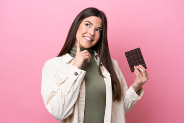 Young Brazilian woman with chocolat isolated on pink background thinking an idea while looking up