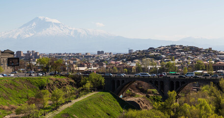 Yerevan, Armenia - April 2022: The park with a river, a bridge with cars and the mountain of Ararat...