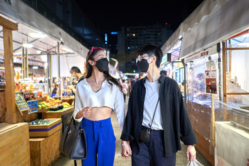 Homosexual couple in mask walking relaxed through an urban night fair