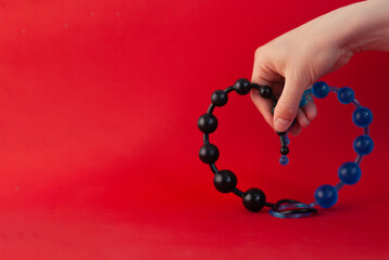 Close-up of female hands holding anal beads of black and blue color on the red background. Anal...