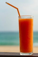 Tropical drink juice - fruit papaya mango juice in glass with tubule, ocean beach.