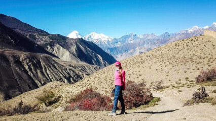 A woman enjoying the view on dry Himalayan valley, located in Mustang region, Annapurna Circuit Trek in Nepal. In the back there is snow capped Dhaulagiri I. Barren and steep slopes. Harsh condition.