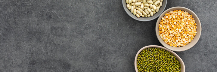 Banner of different types of legumes in bowls, yellow peas and chickpeas , colored beans and maash and lentils, top view, copy space
