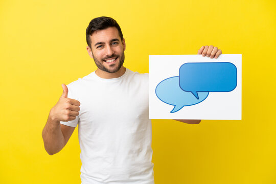Young handsome caucasian man isolated on yellow background holding a placard with speech bubble icon with thumb up