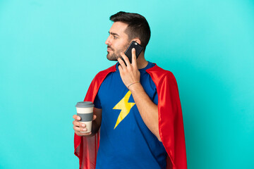 Super Hero caucasian man isolated on blue background holding coffee to take away and a mobile © luismolinero