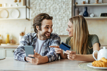 Glad surprised european millennial family with phone and credit card, blonde wife pointing finger...