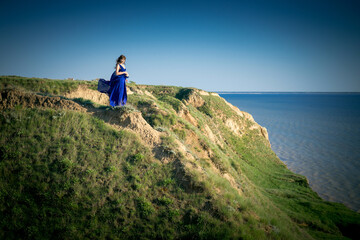 girl in a beautiful dress on a cliff above a precipice. A girl in a blue dress is sitting on the edge on the edge of the cliff . Extreme girl. Photoshoot, Ukraine, Stanislav Canyon . 