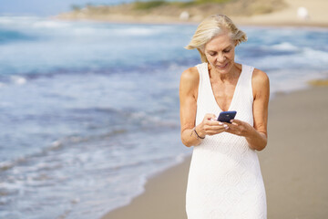 Fototapeta na wymiar Mature female walking on the beach using a smartphone.