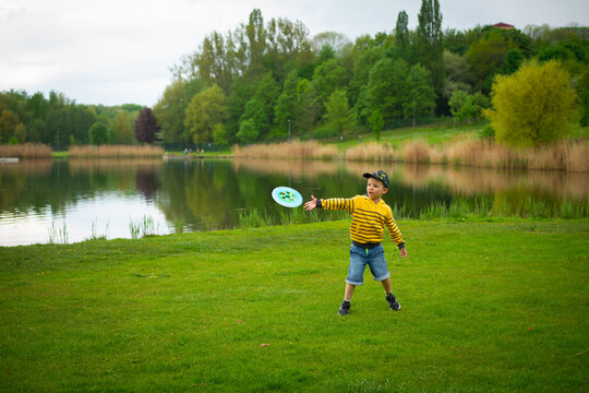 Little cute boy plays frisbee in the park against the background of green grass.