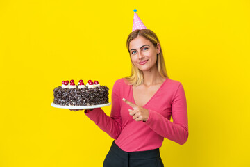 Blonde Uruguayan girl holding birthday cake isolated on yellow background pointing to the side to...