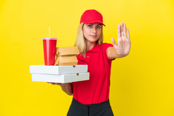Delivery Uruguayan woman holding fast food isolated on yellow background making stop gesture