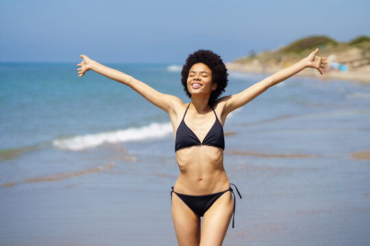 Cute black woman opening her arms on the beach to enjoy her holiday in the sun.