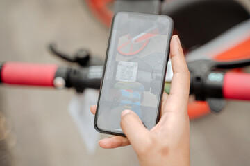 Close up of woman hand using mobile app, scanning QR code for rental electric scooter, selective focus. Eco transport concept