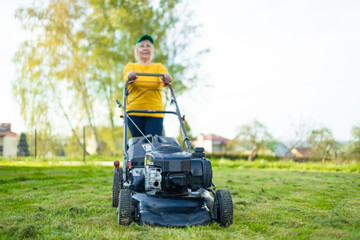 Mowing the grass with a lawn mower in early spring or summer. Gardener woman cuts the lawn in the garden. Worker mowing tall grass with electric or petrol lawn trimmer in city park or backyard.