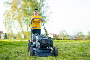 Mowing the grass with a lawn mower in early spring or summer. Gardener woman cuts the lawn in the...