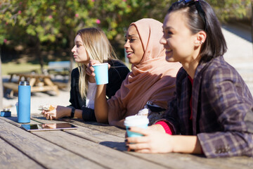 Cheerful diverse ladies having coffee break and chatting in city park