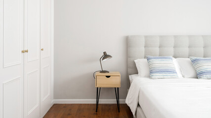 Side table with lamp standing close to bed and wardrobe