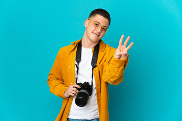 Young  caucasian photographer man isolated on blue background happy and counting three with fingers