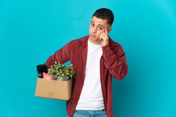 Young caucasian man making a move while picking up a box full of things isolated on blue background...