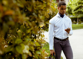 Young African American businessman using a mobile phone while walking on a a street
