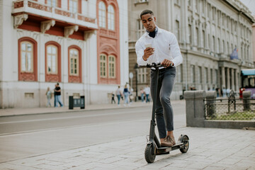 Young African American using mobile phone while standing with electric scooter on a street