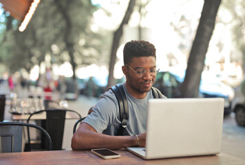 young man uses a computer sitting in an outdoor cafe