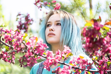 Obraz na płótnie Canvas Portrait of blue haired woman against pink blossom trees at sunny day.