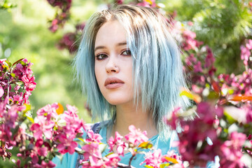 Naklejka premium Portrait of blue haired woman against pink blossom trees at sunny day.
