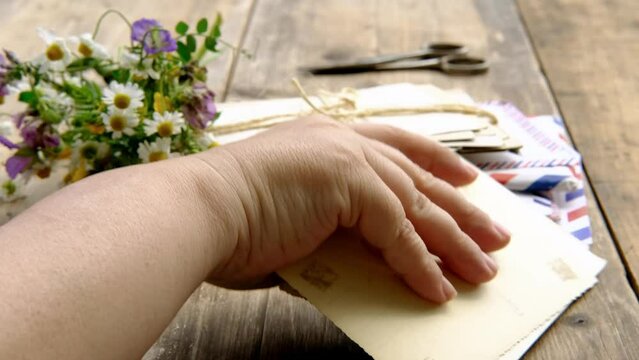 female hands holding paper envelope with old photographs, bouquet of wild flowers on table wooden table in garden, blurred natural background, concept of genealogy, memory of ancestors, family tree
