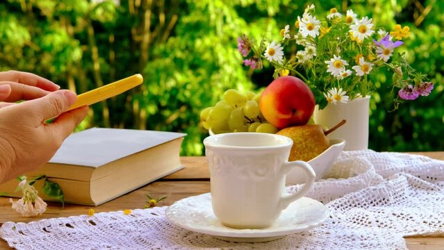 tea, coffee in white mug on saucer, female hand hold smartphone with blank screen mobile, fruits, book, lace napkin, bouquet of wild flowers on wooden table, concept tea time, technology in everyday