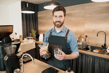 Handsome man with coffee mugs in her hands standing behind counter in cafeteria