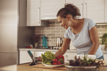 A woman in the kitchen stands at the table ready for cooking salad for a blog using a tablet
