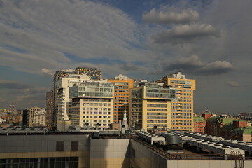Fototapeta premium Panorama of the city with modern high-rise residential complexes, roofs of buildings and expressive clouds in the blue sky.