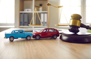 Two small cars on table in courtroom. Gavel and little toy car models on desk in courthouse. Road crash, law, justice, lawyer services, civil trial, accident case study, insurance coverage concept